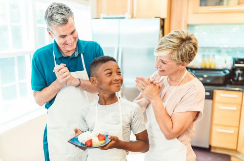 boy holding a plate of pancakes beside a couple in the kitchen