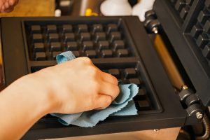 close-up of a hand wiping a waffle maker with a blue cloth