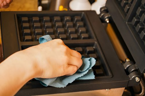 close-up of a hand wiping a waffle maker with a blue cloth